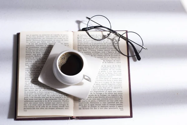 white cup with Colombian coffee on a book and round glasses