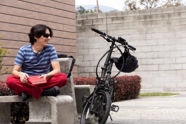 Man smiling while on his break time while looking at his electric bike and reading in his spare time
