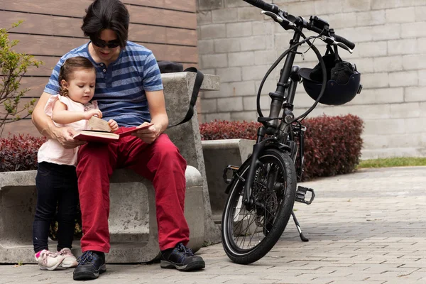 Man and girl reading outside sitting in a cement chair next to his electric bike