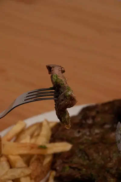 Fork in the foreground with a piece of meat and in the background out of photo the rest of the plate