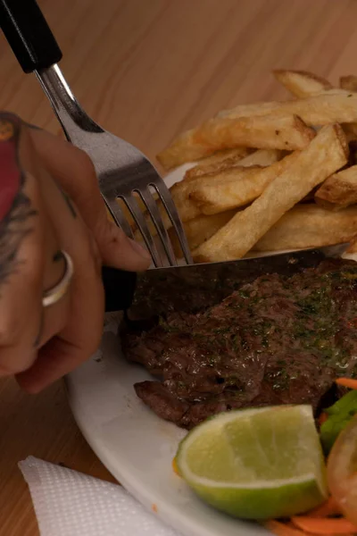 Woman\'s hand with fork and knife slicing meat at lunch time