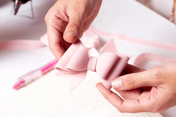 Bir kadının elleri el işi masasında deri kumaştan yapılmış pembe bir yayı kontrol ediyor.