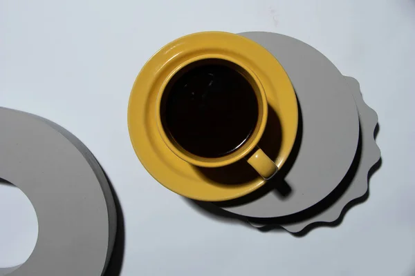 Żółta Filiżanka Kawy Obok Szarych Figur Geometrycznych Twardego Światła — Zdjęcie stockowe
