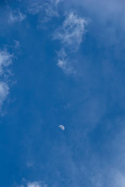 Blue sky with diffuse clouds and the moon in the middle during the day