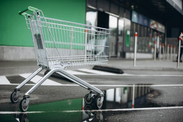 A supermarket basket is on the asvalt and a puddle of water, a wheelchair — Stock Photo, Image