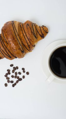 Üst ya da düz kahve fincanı ve kruvasanla beyaz arka planda fotokopi alanı. Sabah kahvesi ve atıştırmalık.