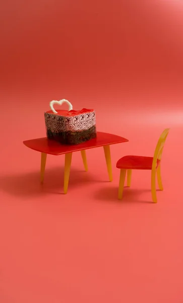 Üzerinde beyaz çikolata kalp olan çikolatalı kek, pembe arka planda mesaj için yer var. Sandalyedeki oyuncak masasında pasta. Sevgililer günü, kartpostal.