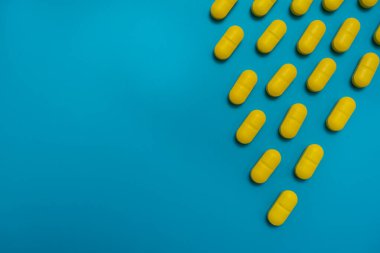 Sarı vitamin ilaç kapsülleri mavi arka planda izole edilmiş haplar. Sağlık konsepti, uyuşturucu ve tehlike.