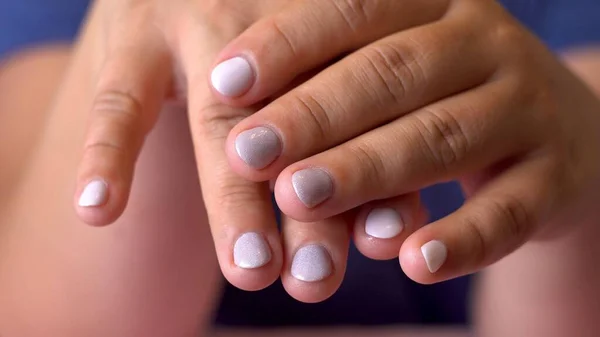 Women\'s hands. Light varnish on the nails. Manicure. Dark skin. Chubby fingers. Blue clothes. Pink towel. Part of the body. Close-up.