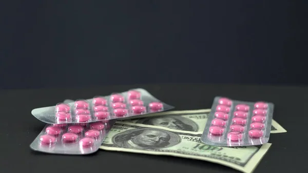 Pink pills in shiny packaging. American dollars. Black background. Treatment. The course of therapy. Medicine. Pharmacology. Tablet production. Pharm industry. Business. Pharmacy.