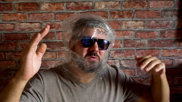 A plastic bag is worn on the head. The man has dark glasses. Cheerful view. The man is dancing. Halloween holiday. Party. Ecology problems. Against the background of a brick wall. Close-up.