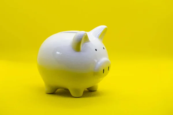 White piggy Bank on a yellow background and human hand putting coin in piggy bank for saving money wealth and finance concept and the copyspace for design.