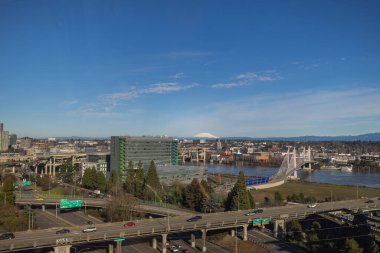Portland, Oregon şehir manzaralı ve arkasında Adams Dağı var. Şehir yüksek binalar, köprüler ve ağaçlarla dolu. Arabalar caddelerde ve köprülerde ilerliyor..