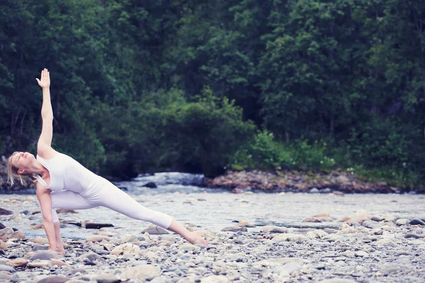 Молода жінка практикує йогу на кам'яному березі річки — стокове фото