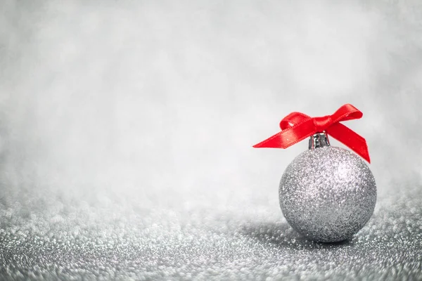 Christmas holiday composition of festive decor ball with red ribbon bow on silver glitter bokeh background