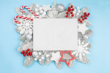 Şekerli köknar ağacı dalları ve mavi zemin üzerinde noel dekoratif süsleme topları ve metin şablonu için kopyalama alanı olan beyaz dikdörtgen kart düz görünüm dizaynı yatıyordu