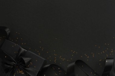 Kara Cuma hediyesi, ipek kurdele yaylı kağıt kutu ve siyah kağıt zemin üzerinde altın parıltılı yıldızlar metin için kopya alanı, düz üst görünüm şablonu yatıyordu