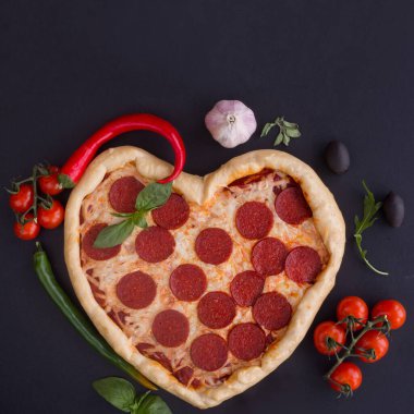 Siyah arka planda içeriği olan pepperoniyle şekillendirilmiş pizza kalbi. Sevgililer Günü için romantik aşk kavramı. Aşk yemeği.