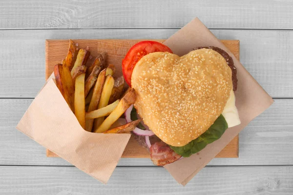 Heart shape love hamburger and french fries, burger fast food concept, Valentines day surprise dinner, wooden background, top view flat lay