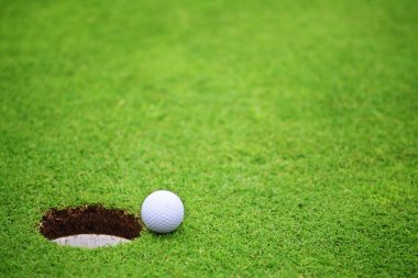 Deliğe yakın golf topu, fincanın dudağında golf sahası arka planında metin pankartı için fotokopi alanı