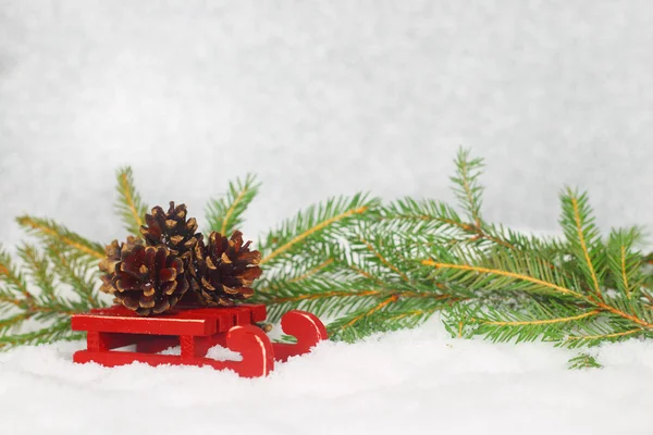 Tarjeta de Navidad con conos de pino en trineo de pie sobre la nieve con ramas de abeto — Foto de Stock