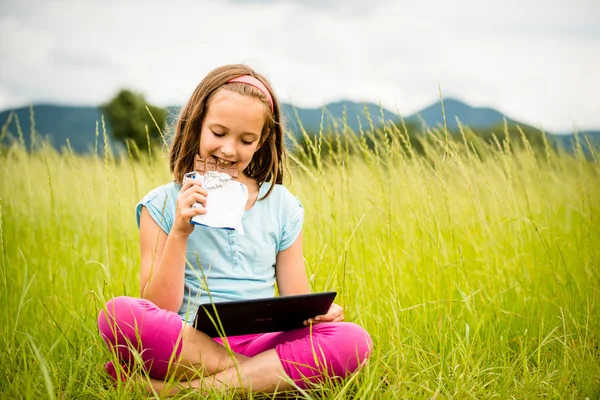 Menina gostando de chocolate e assistir tablet — Fotografia de Stock