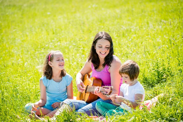 Mother playing guitar in nature to children — Stock Photo, Image