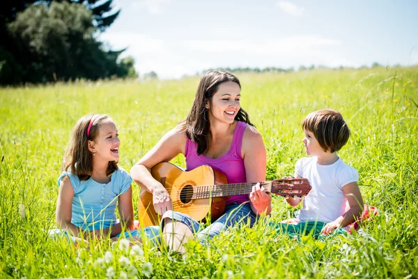 Mother playing guitar in nature to children — Stock Photo, Image