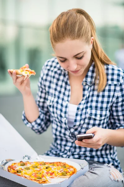 Tinédzser látszó telefon pizzát eszik — Stock Fotó