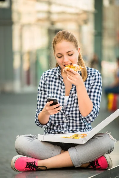 Teenager eating pizza looking in phone — Stock Photo, Image