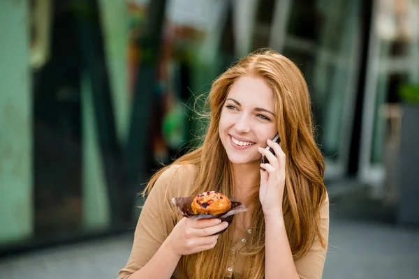 Adolescente comiendo magdalena mirando en el teléfono —  Fotos de Stock