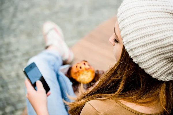 Teenager eating muffin looking in phone — Stock Photo, Image