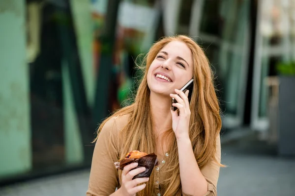 Teenager eating muffin looking in phone — Stock Photo, Image