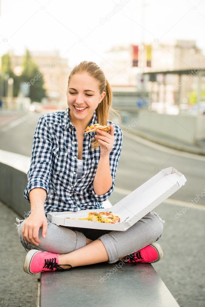 Teenager eating pizza in street