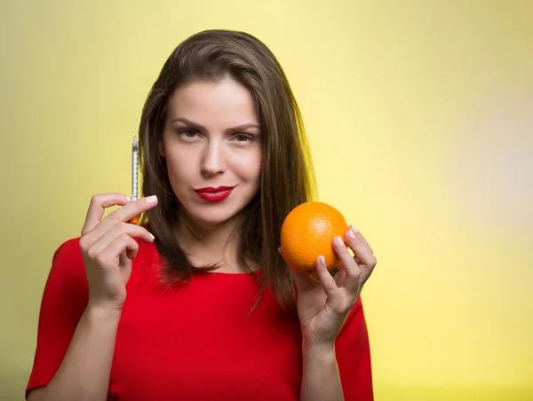 Mujer sosteniendo una jeringa y una naranja — Foto de Stock