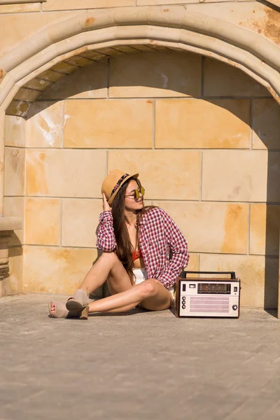 Schöne junge Boho-Frau mit einer Retro-Stereoanlage, die auf einer Saite sitzt — Stockfoto