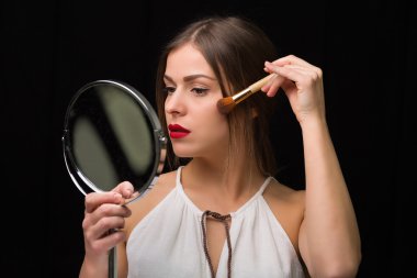 Kadın bir ayna ve makyaj fırça ile