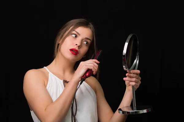 Mulher com um espelho e ferro cabelo liso — Fotografia de Stock