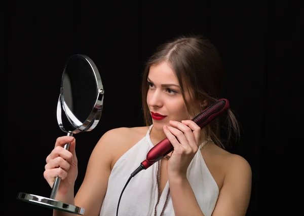 Mulher com um espelho e ferro cabelo liso — Fotografia de Stock