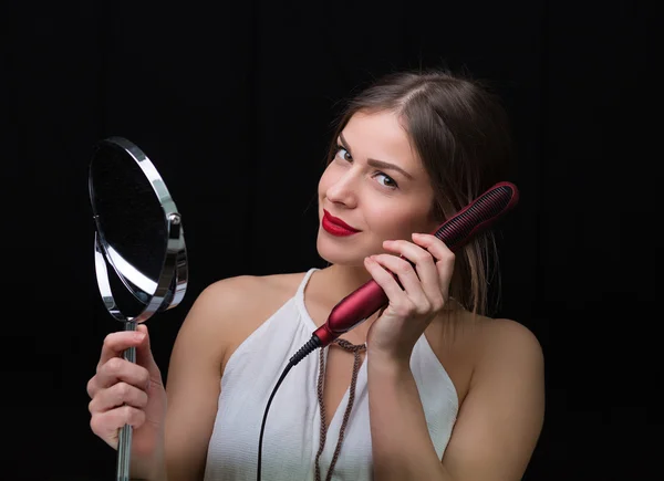 Женщина с зеркалом и утюгом для волос — стоковое фото