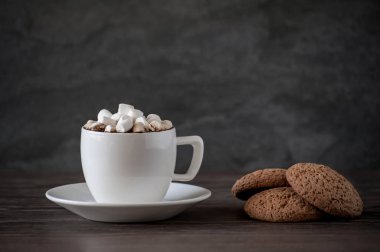 Marşmelovlu bir fincan kahve ve ahşap bir masada yulaf ezmeli kurabiye.