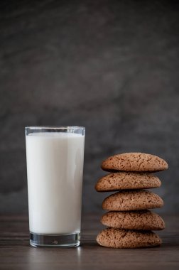Bir bardak süt ve yulaf ezmeli kurabiye, arka plandaki ahşap masada.