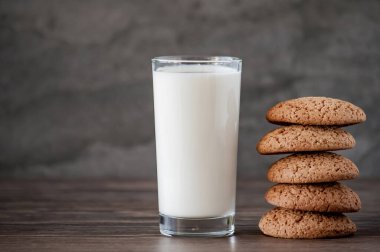Bir bardak süt ve yulaf ezmeli kurabiye, arka plandaki ahşap masada.