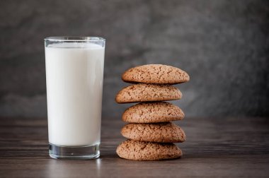 Bir bardak süt ve yulaf ezmeli kurabiye, arka plandaki ahşap masada.