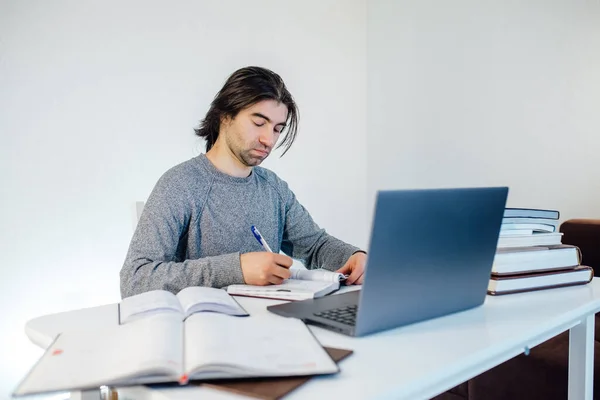 Man student write in notebook working on computer. Internet marketing, freelance work, working from home, online learning, studying, lockdown concept. Distance education, books on the table