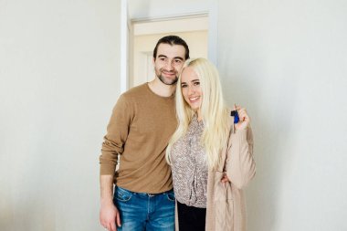 Kafkasyalı genç çift anahtarlarını gösteriyor ve kameraya bakıyor, kucaklaşıyorlar, mutlu aile taşınma gününü kutluyorlar, yeni eve taşınıyorlar, mülk sahipleri,
