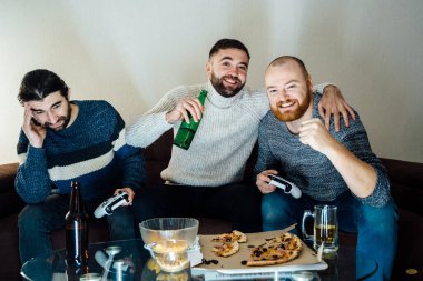 Kablosuz kontrolörlerle video oyunu oynayan üç mutlu sakallı adamın görüntüsü. joystickle video oyunlarında yarışan üç arkadaş,