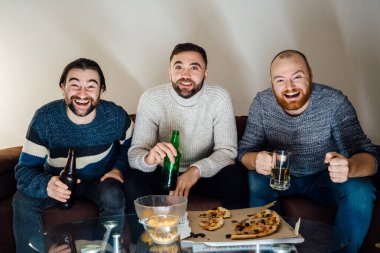 Heyecanlı arkadaşlar oturma odasında toplanıp TV 'de harika bir program izliyorlar. Elinde birayla kanepede oturan üç adam TV 'de komedi izliyor..