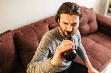 Depresyonda olan, biradan bira içen, yatakta düşünceli ve kafası karışmış alkolik, alkolik ve alkol bağımlısı genç bir adam.