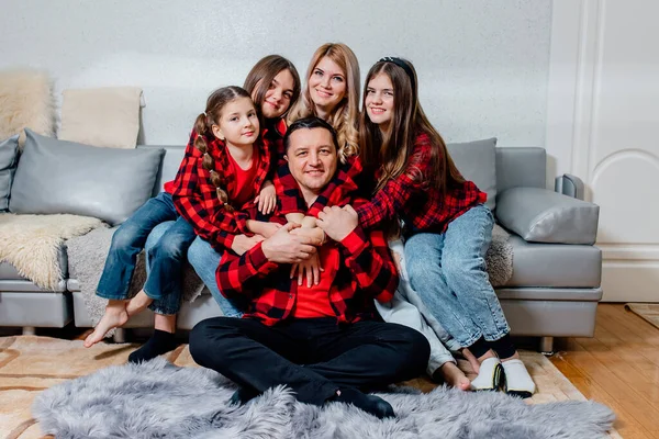 happy family dressed in red shirts with squares. three daughters mother and father. the whole family looks at the room.